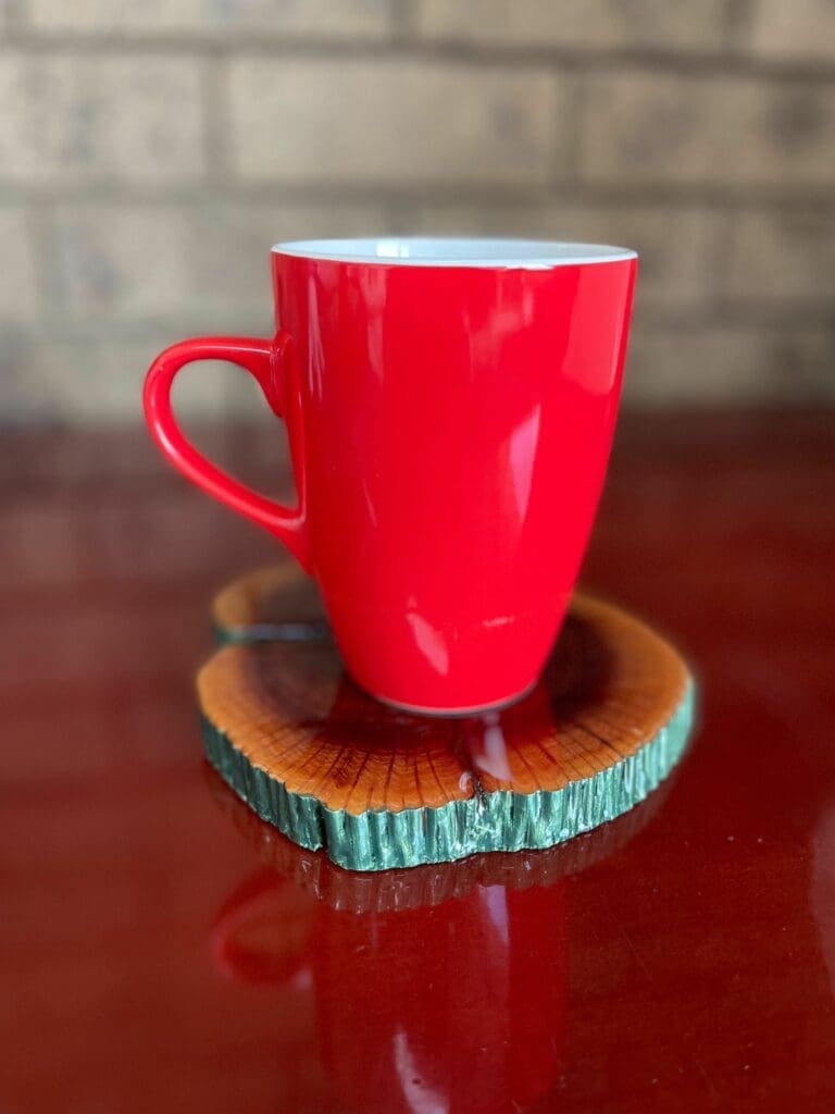 Bright red ceramic mug resting on a glossy resin coaster made from a tree-slice with green-painted bark edge — Stone Coat Art Coat finished piece